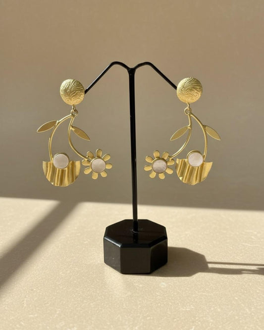 Gold floral earrings on a black stand against a beige background