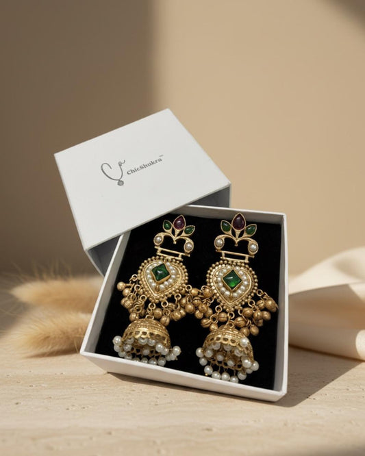 Gold earrings with green gemstones in a white box on a beige background