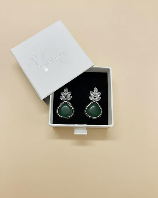 Green teardrop earrings with silver leaves in a white box on a beige background