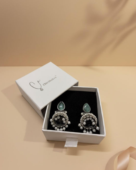 Pair of earrings in a white box on a beige background