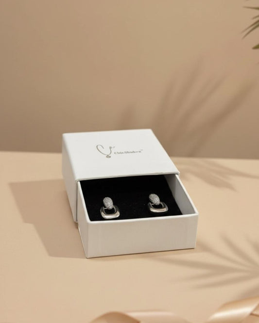 Silver earrings in a white jewelry box on a beige surface