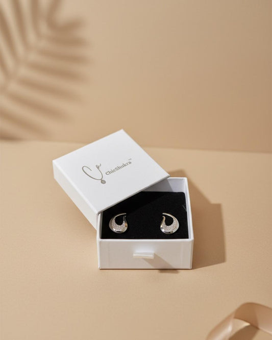 Silver earrings in a white box on a beige background