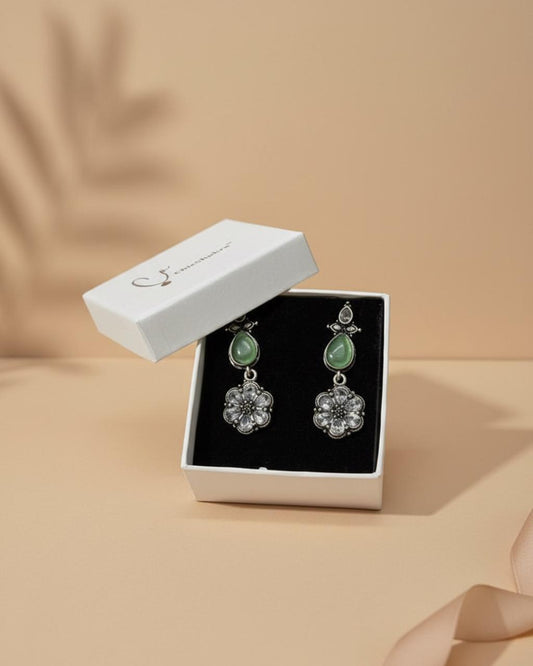 Pair of earrings with green gemstones in a white jewelry box on a beige background