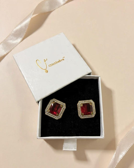 Red square earrings with gold accents in a white box on a beige background