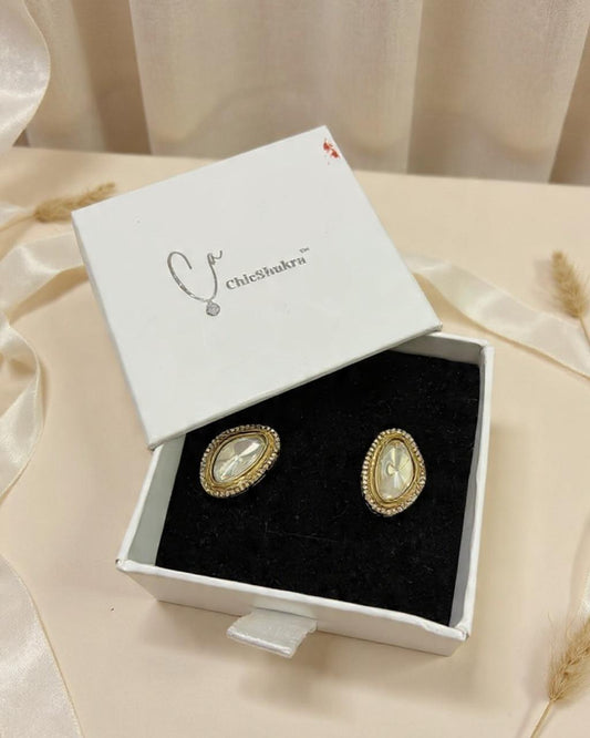 Gold earrings in a white box with 'Chic Shakti' branding on a beige fabric background