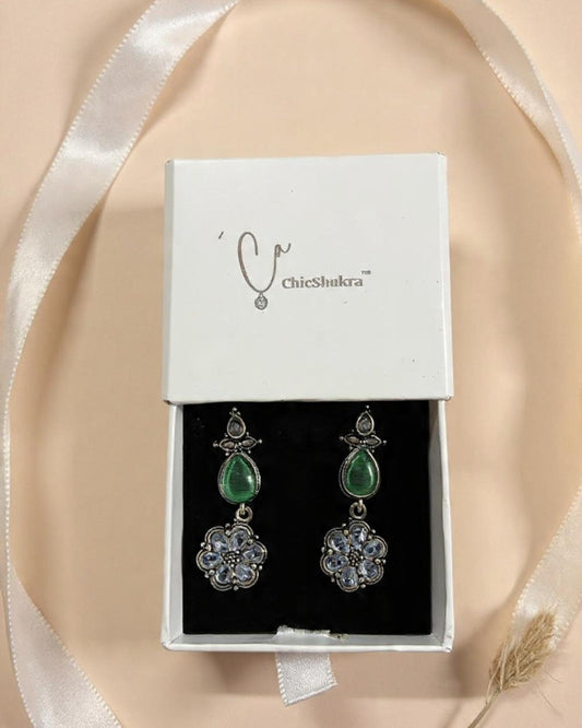 Pair of earrings in a white box with 'chicShukra' branding on a beige background.