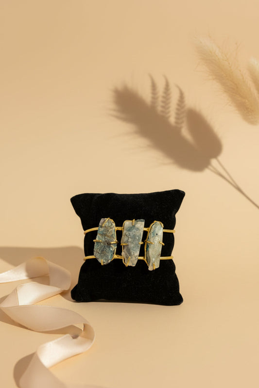 Jewelry set with three green stones in gold settings on a black pillow against a beige background.
