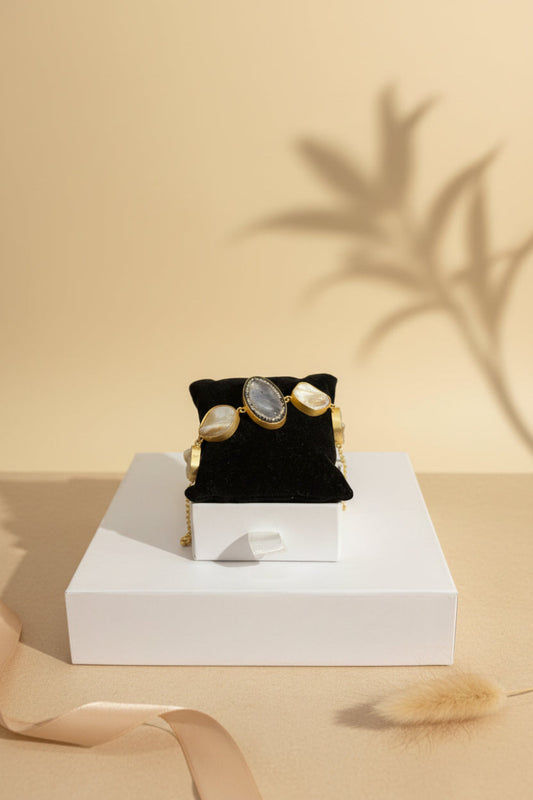 Gold bracelet with a central stone on a black velvet stand against a beige background