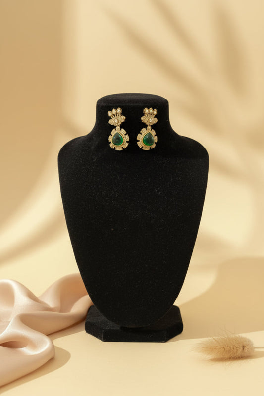 Gold and green earrings on a black velvet stand with a beige background