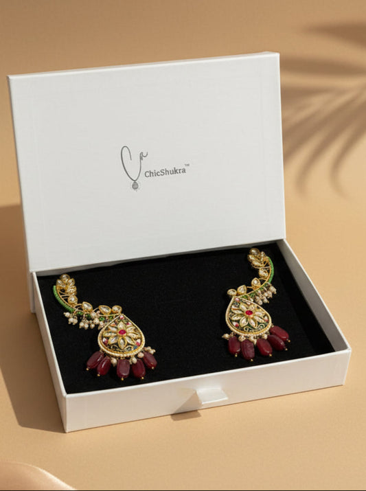 Ornate earrings with red stones in a white box on a checkered background