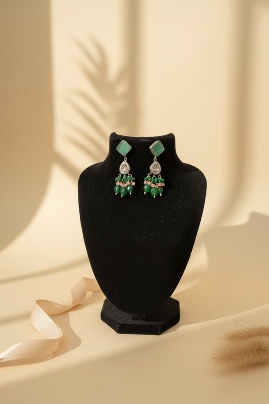 Pair of green and pink beaded earrings on a black stand.