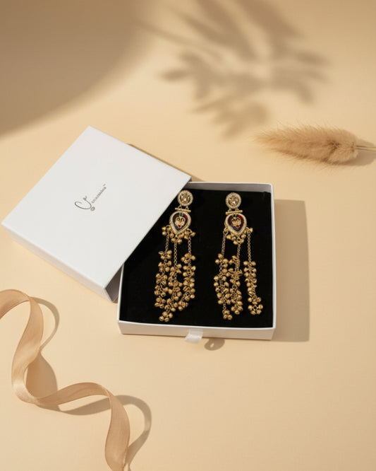 Gold earrings in a box on a floral-patterned fabric background