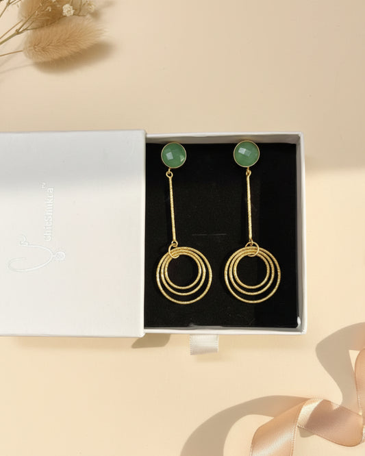 Gold hoop earrings with green stones in a Chichakala box on a floral fabric background