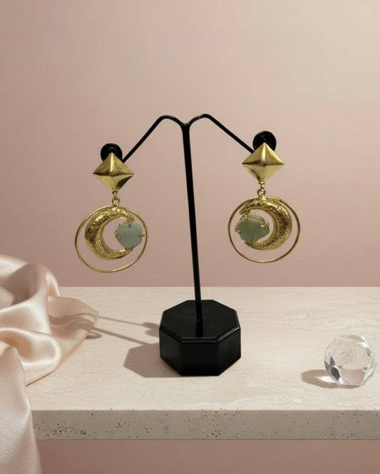 Gold earrings on a black stand against a pink background