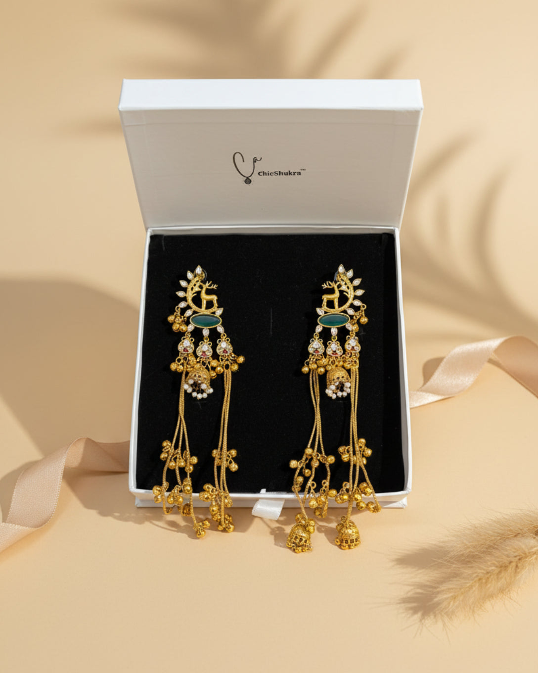 Gold earrings with intricate designs on a black cushion inside a ChicShukra box.