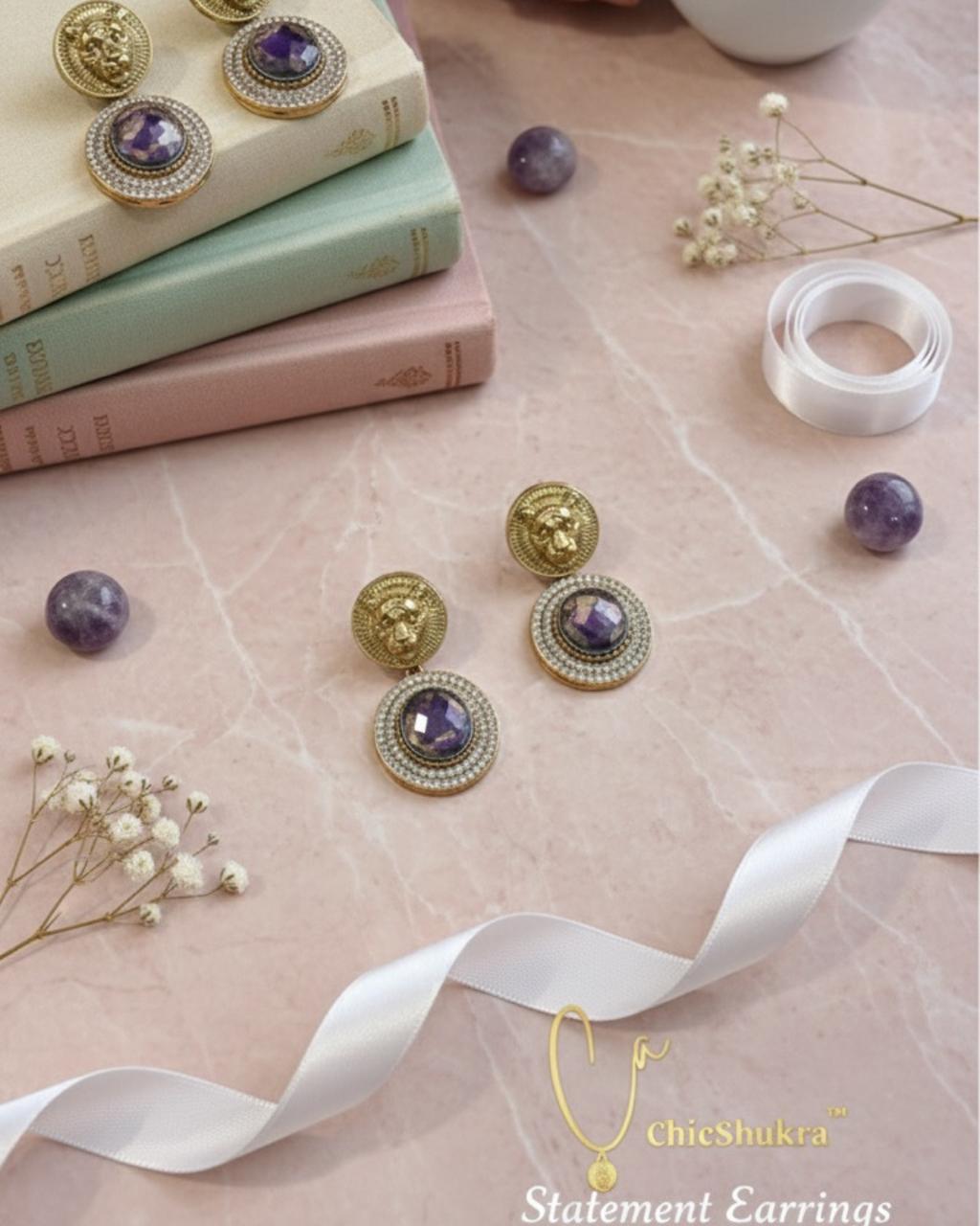 ChicShukra brass statement earrings with purple amethyst and rhinestone detailing on marble surface with books and ribbons