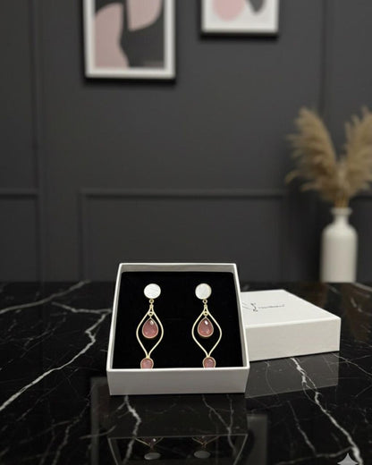 Pair of earrings in a white box on a dark marble surface with a gray wall in the background.