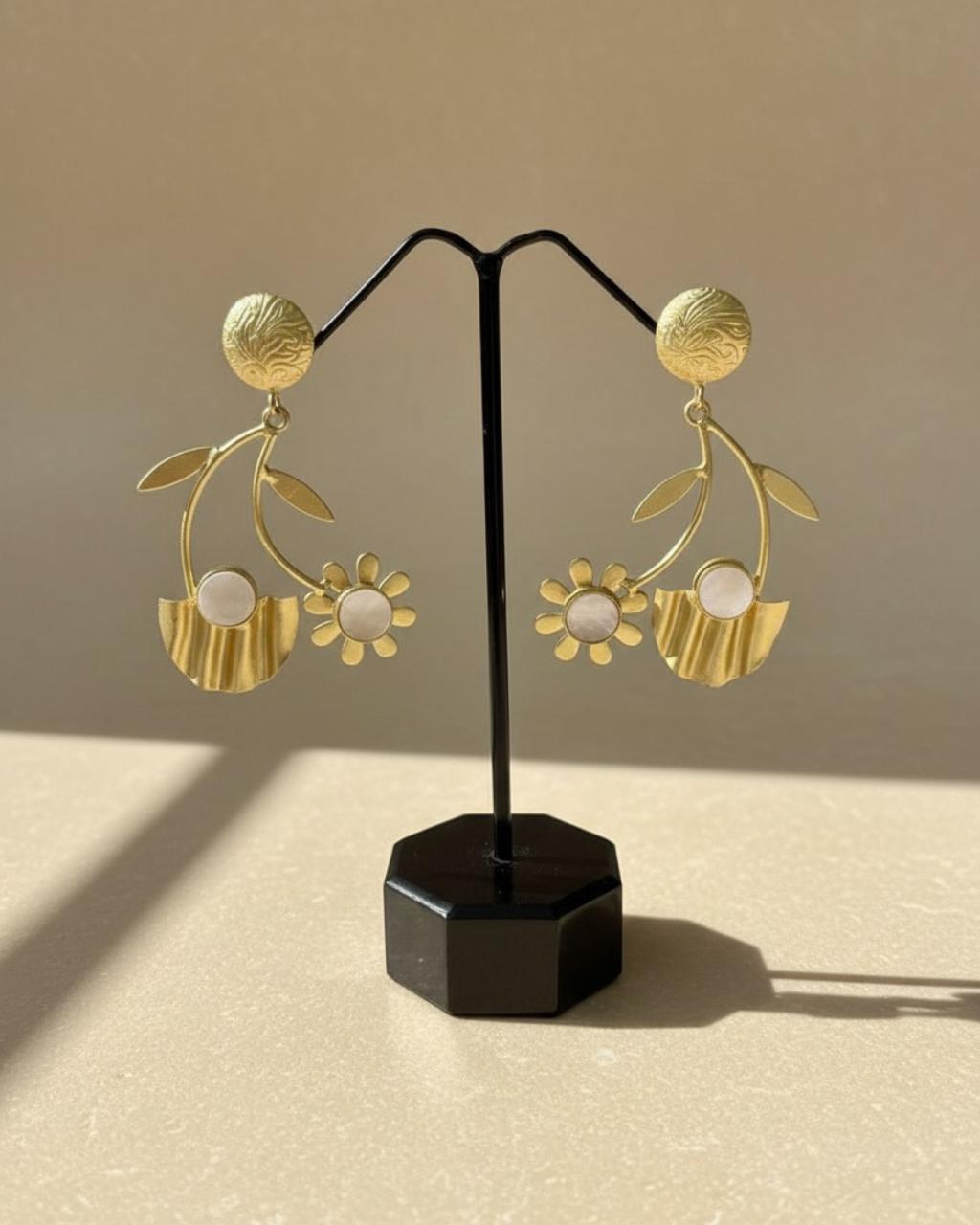 Gold floral earrings on a black stand against a beige background