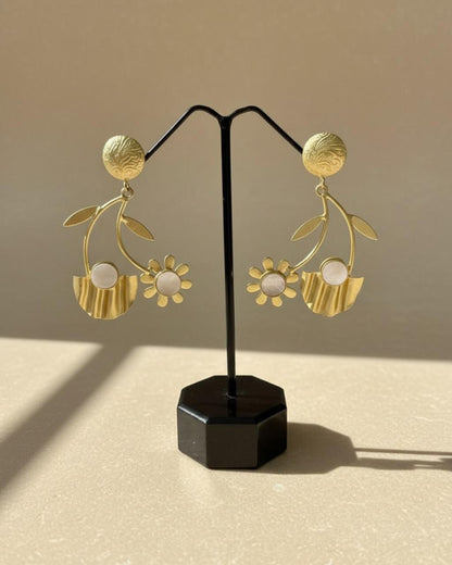 Gold floral earrings on a black stand against a beige background