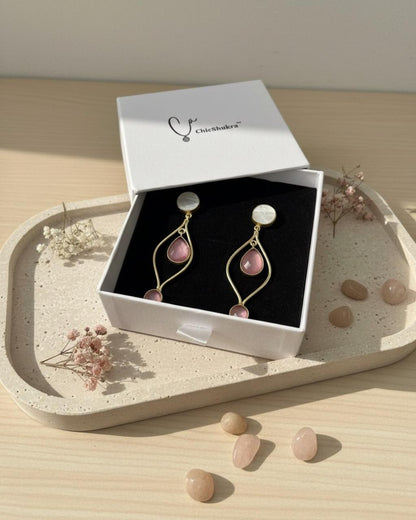White jewellery box with ChicShukra brass earrings featuring pink rose quartz and white pearl studs on a concrete tray with flowers and stones.
