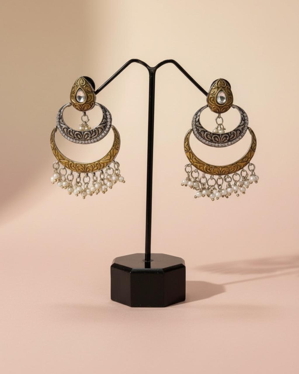 Pair of ornate earrings on a black stand against a beige background