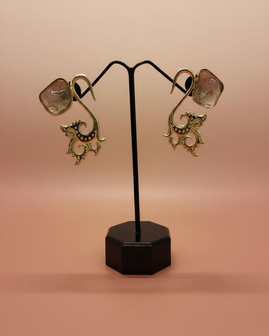 Pair of gold earrings on a black stand against a pink background