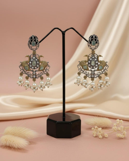 ChicShukra peacock design imitation jewellery earrings with green stones, diamond accents, and pearl drops on a black display stand