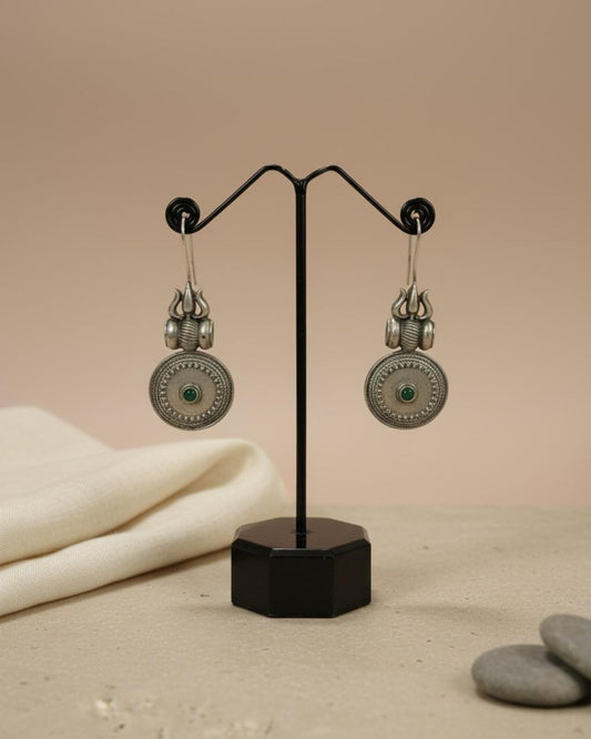 Pair of silver earrings with green stones on a black stand against a beige background