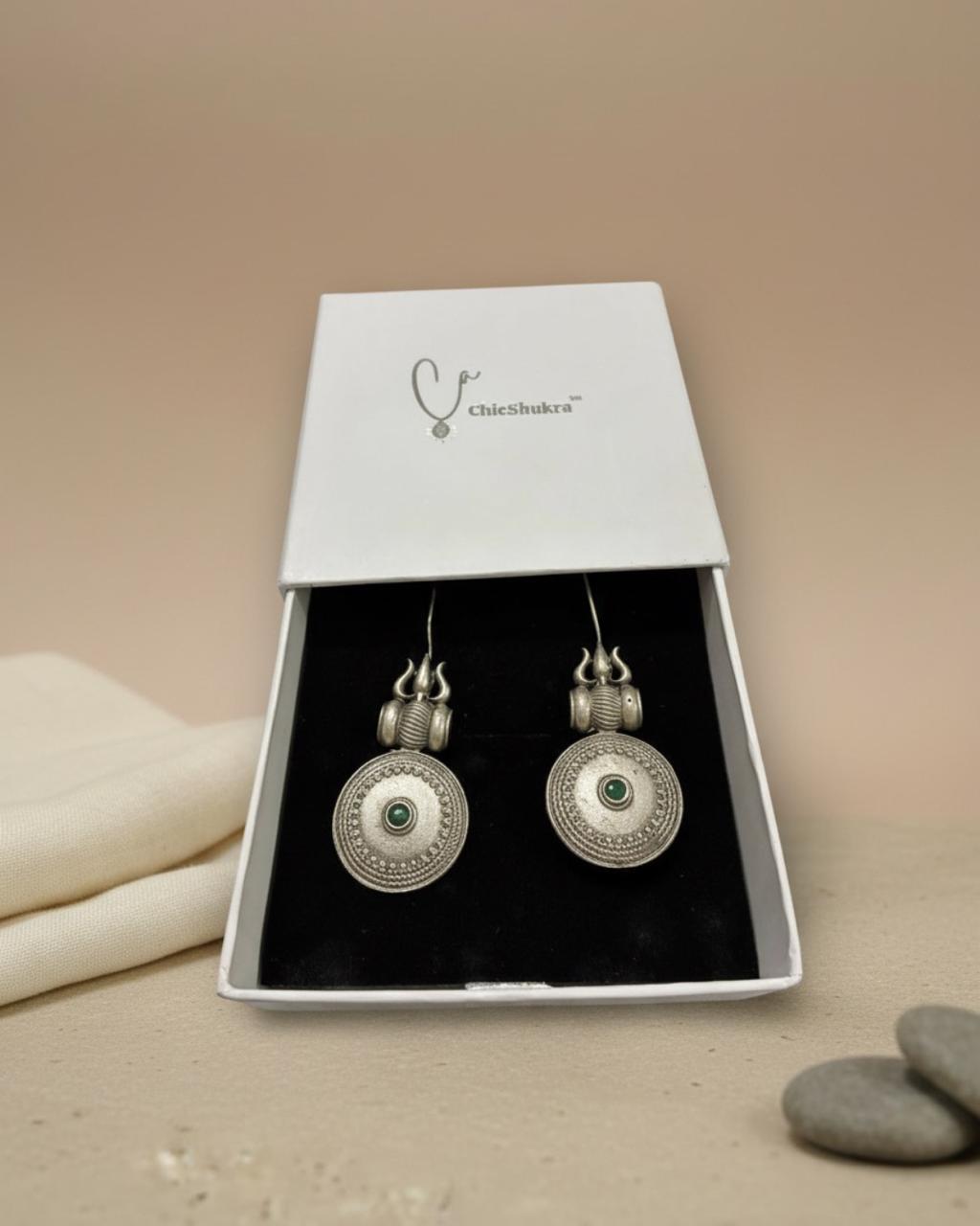 Silver earrings with green gemstones in a Chichikaka box on a beige background