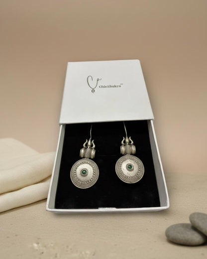 Silver earrings with green gemstones in a Chichikaka box on a beige background