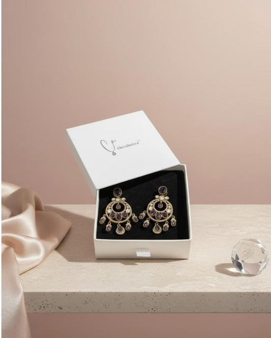Gold earrings with black center in a white box on a light pink background