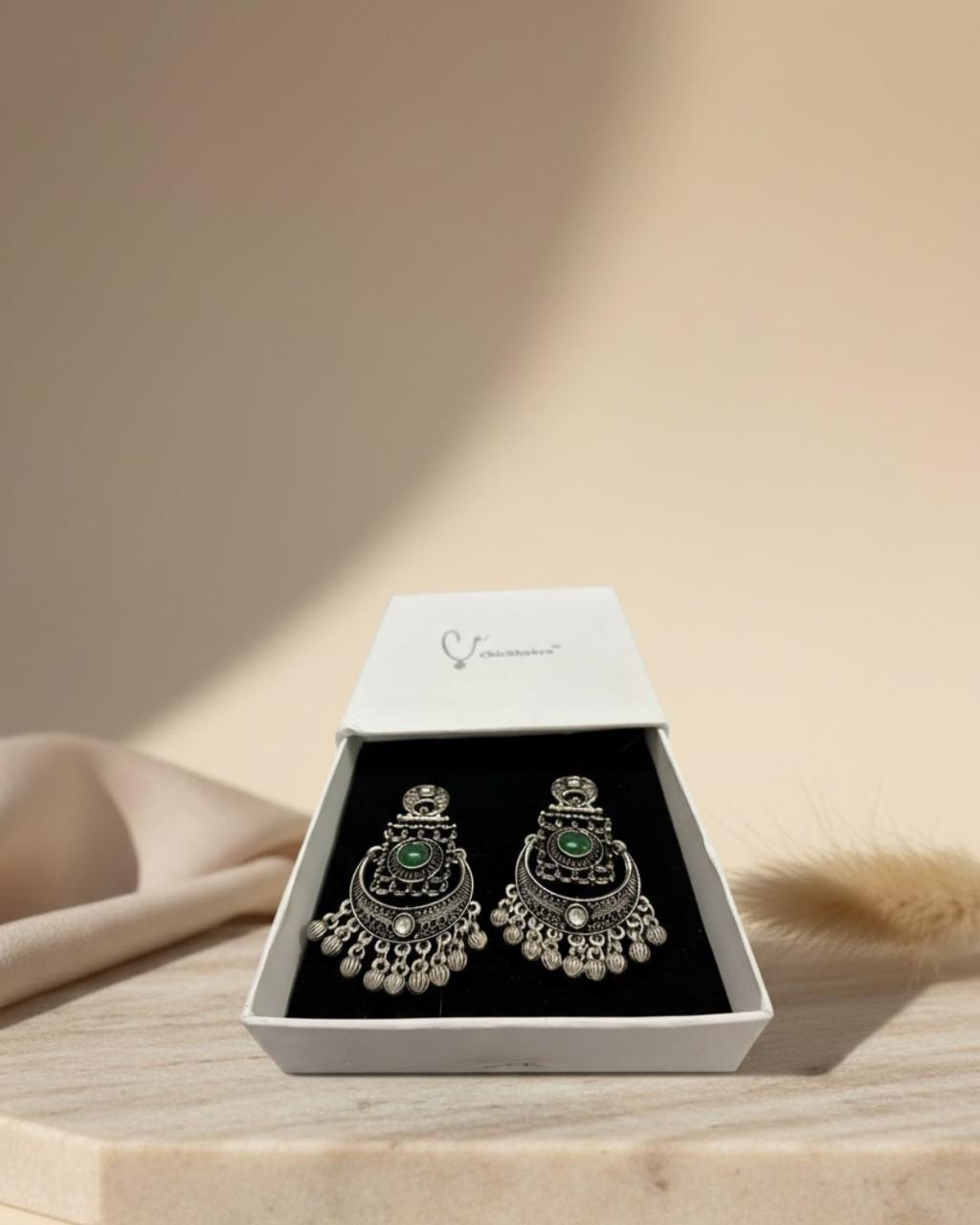 Ornate earrings in a white box on a wooden surface with a soft beige background