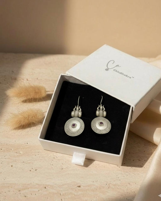 Silver earrings in a white box on a wooden surface with a soft focus background