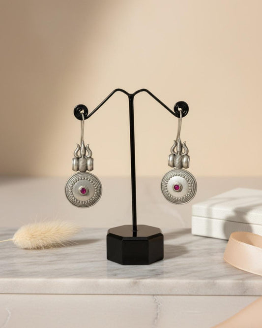 Pair of silver earrings with gemstones on a black stand against a beige background