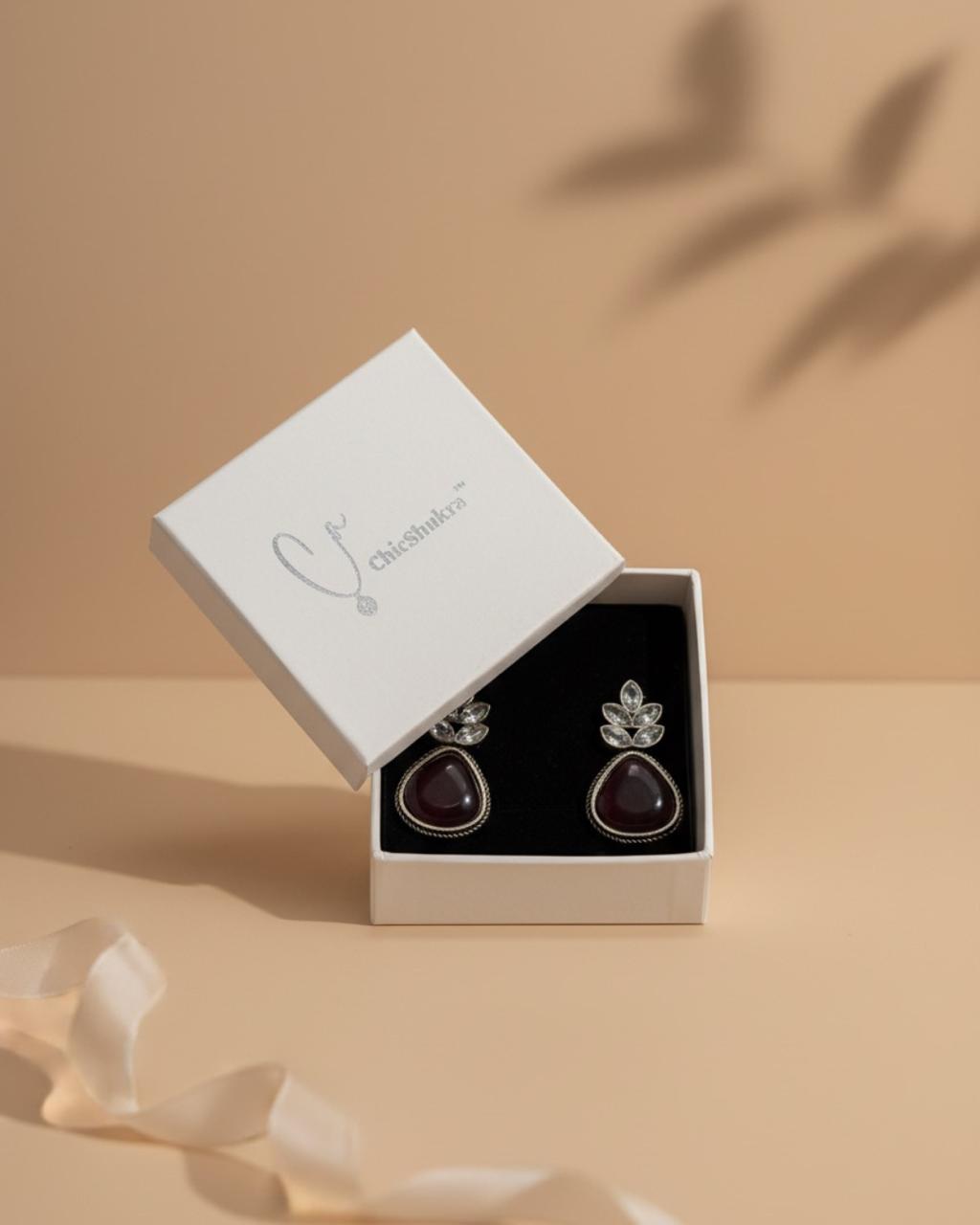 Pair of earrings in a white box on a beige background