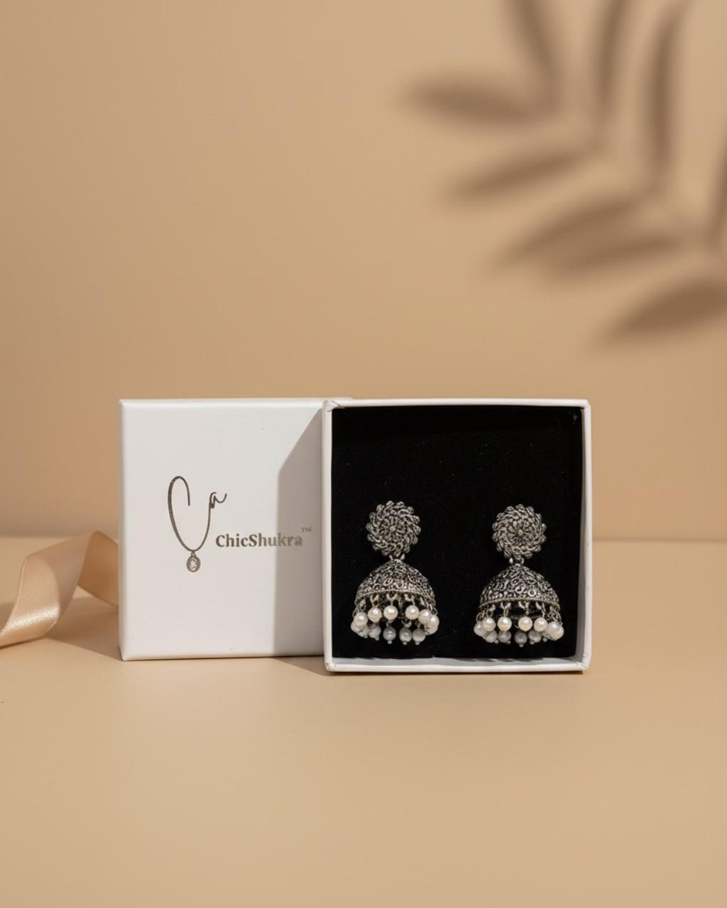 Silver‑toned ChicShukra brass jhumka earrings with pearl beads in a white gift box.