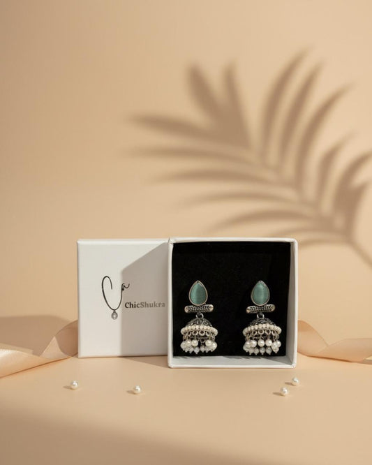 A pair of ChicShukra mint green stone and pearl jhumka earrings in a white jewelry box with the brand logo "ChicShukra"