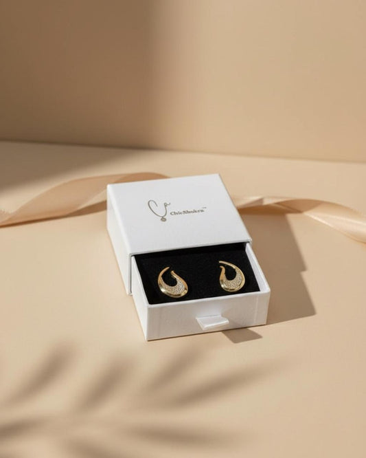 Gold earrings in a white box on a beige fabric background