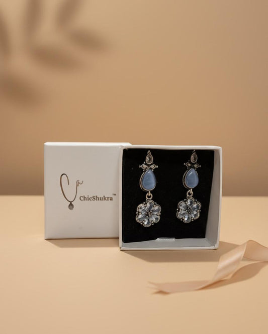 ChicShukra brass earrings with blue pear stone and silver floral crystal pendants in a white gift box.