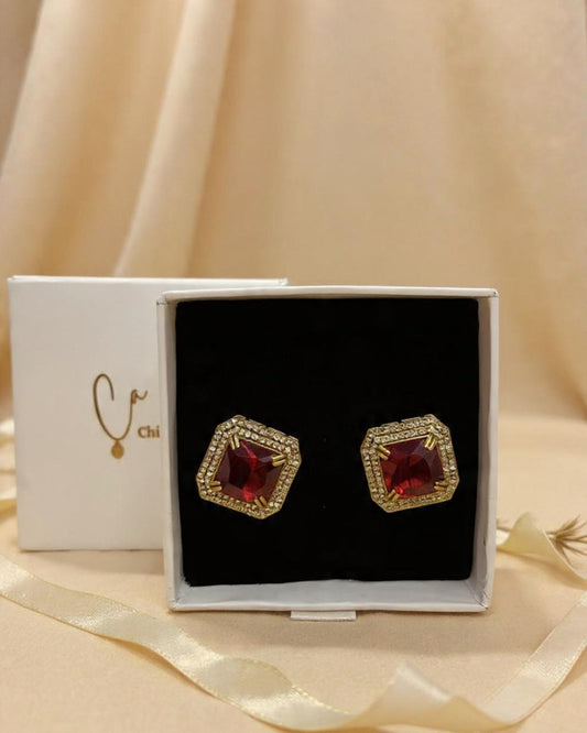 Chicshukra brass earrings with red hexagonal gemstone and gold‑tone diamond halo in a white jewellery box.