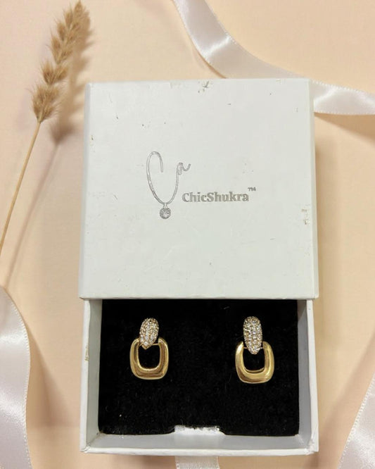 Gold earrings with clear stones in a ChicShukra box on a beige background