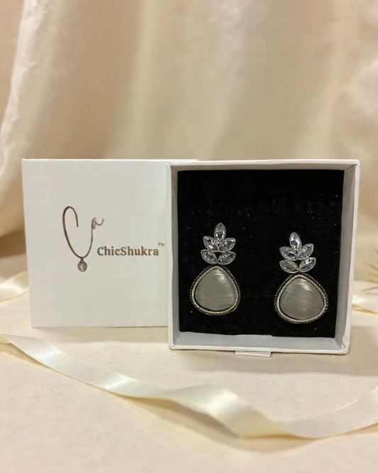 Silver earrings with gemstones in a ChicShukra box on a beige fabric background