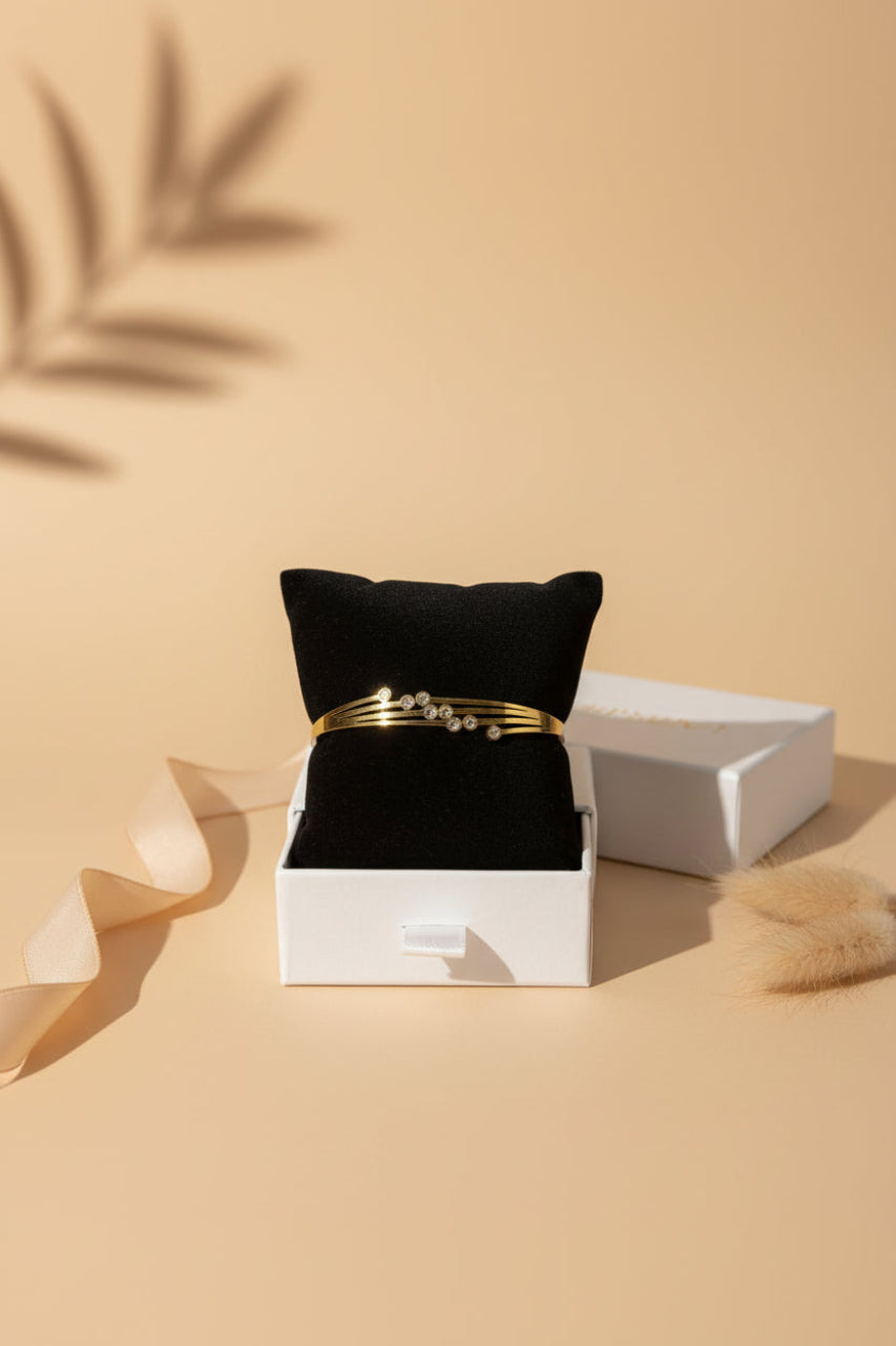 A gold-toned brass bangle with three slender bands and sparkling zirconia stones displayed on a black velvet jewelry box.