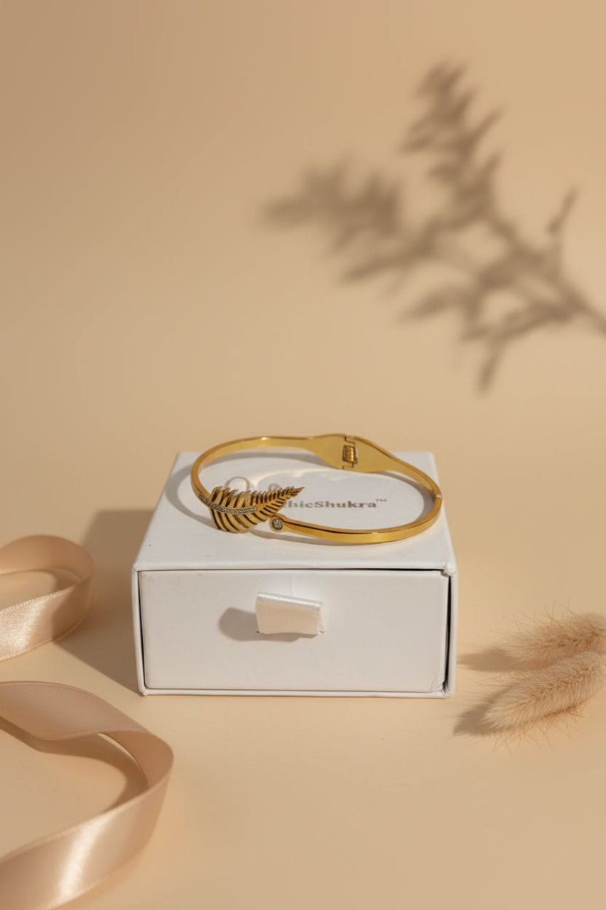Golden fern leaf brass bangle with diamond accents by ChicShukra resting on a white jewellery box.
