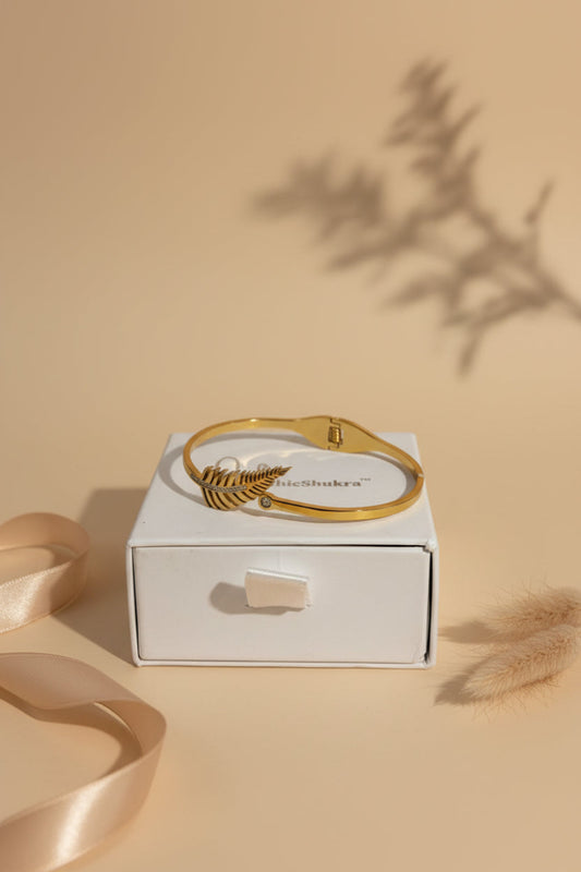 Golden fern leaf brass bangle with diamond accents by ChicShukra resting on a white jewellery box.
