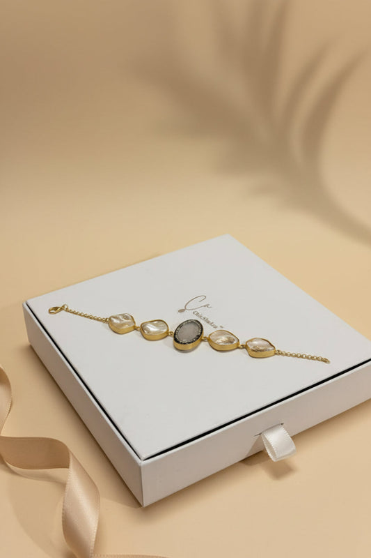 A gold‑plated brass bracelet with five irregular white mother‑of‑pearl stones set in gold bezels, one stone framed with black zirconia, lying on a white jewellery box with the ChicShukra logo.