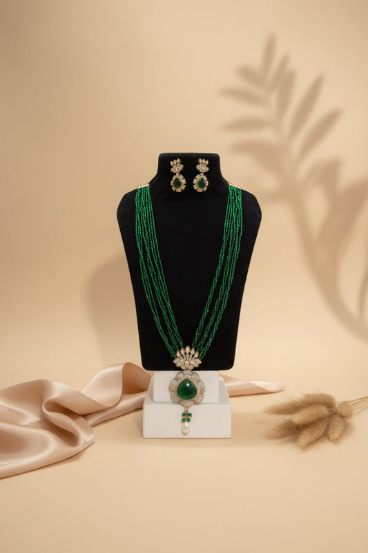 Chicshukra emerald green multi‑strand imitation necklace set with diamond‑studded pendant and matching earrings on black jewelry display.