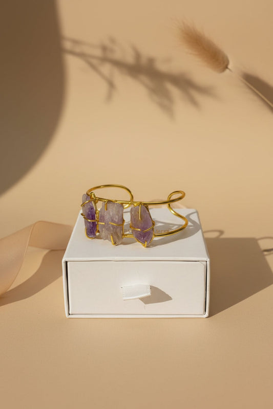 Gold bracelet with purple stones on a white box against a beige background