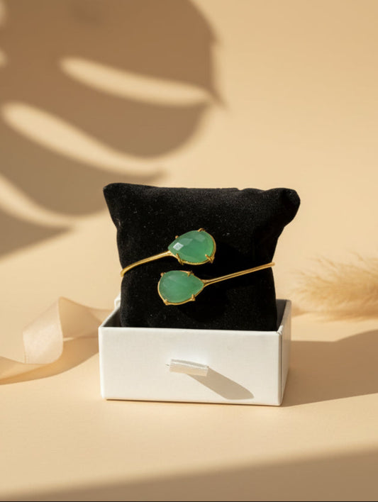 Golden brass open bangle with two emerald green faceted gemstones by ChicShukra, resting on a white jewellery box.