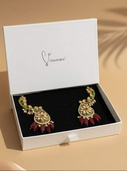 Ornate earrings with red stones in a white box on a checkered background